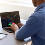 businessman working on laptop, sitting at desk in office, typing on keyboard, trading online, buying or selling bitcoins, cryptocurrency,